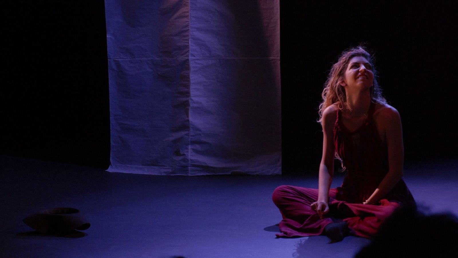 La femme en robe rouge, assise au sol, le regard levé · captation Compagnie AJM, 22 février 2026